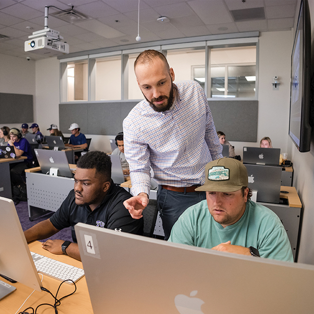 Faculty member looking over student's shoulder at desktop computer